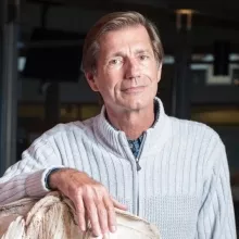 An middle aged man leans on a whale bone and smiles at the camera.