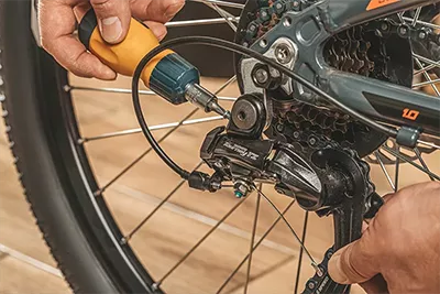A rear bike wheel and a hand holding a screwdriver near the axel.