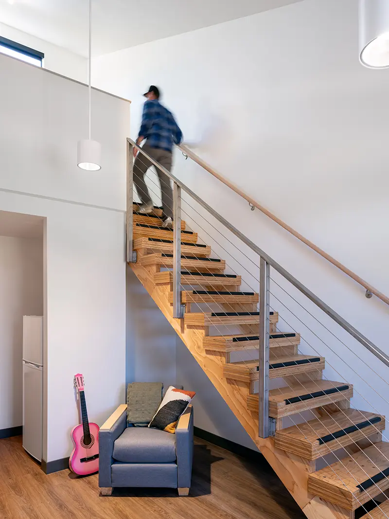 A person is walking up the stairs to a loft. Below is a chair and pink guitar.