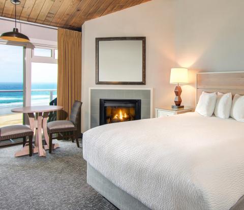 A hotel room with a bed, fireplace and view of the ocean from the window.
