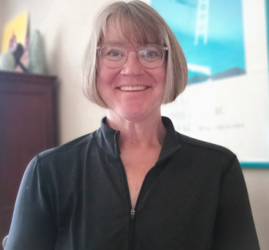 A woman with gray brown chin-length hair and glasses.