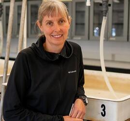 A woman with graying hair and bangs stands in a wet lab.. 