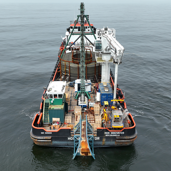 A large vessel with cranes and testing equipment on a still ocean.