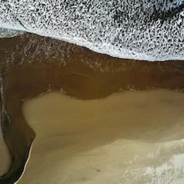 White foamy waves wash up on a sandy beach.
